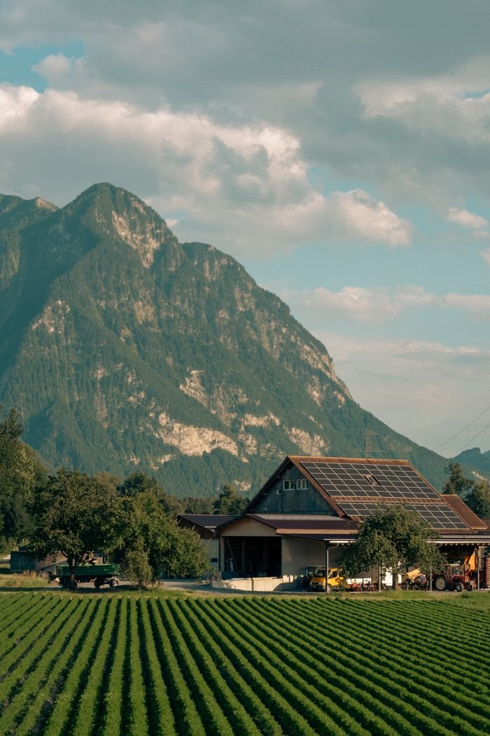 Captivating view of a solar-powered barn amidst lush Swiss fields and alpine mountains.